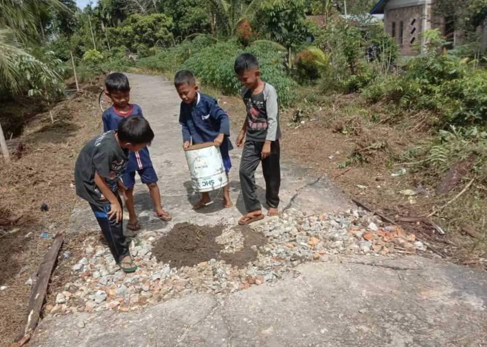 Anak-anak desa setempat ikut bergotong royong menambal jalan Desa Tenan yang rusak parah